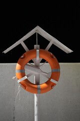 The orange lifebuoy is hanging on a special pole at the seafront.