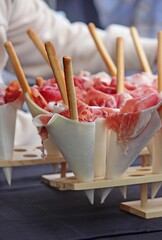 Prosciutto crudo cone and a bread stick cones for sale. Italian street food. Wooden disposable tasing cones.