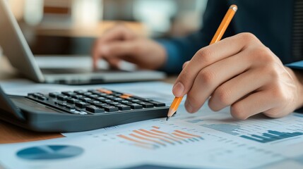 Closeup of a businessman or accountant holding a pencil while working on a calculator to calculate financial data accompanied by accountancy documents and a laptop in an office setting