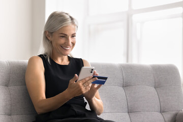 Attractive mature woman engaged in on-line shopping, make transaction using her credit card and...