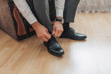 A man is putting on his shoes. He is wearing a watch and is sitting on a chair