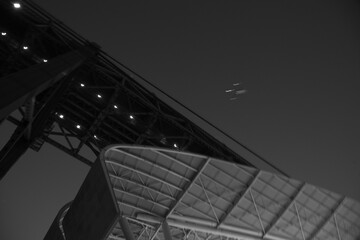 City scene under the 25 of April bridge in Lisbon at dawn with the lights of an airplane flying over in the sky