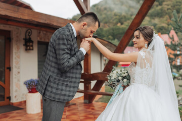 Fototapeta premium A man and a woman are kissing each other's hands. The man is wearing a suit and tie, and the woman is wearing a white dress. They are standing outside in front of a building