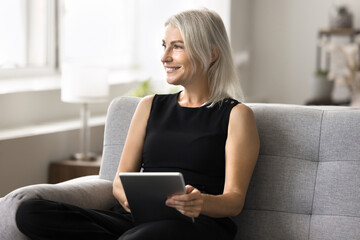 Woman resting on sofa with tablet, communicate with friend via messaging apps, engaging in digital hobby such as drawing, photography or creative writing, enjoy entertainment on weekend using internet