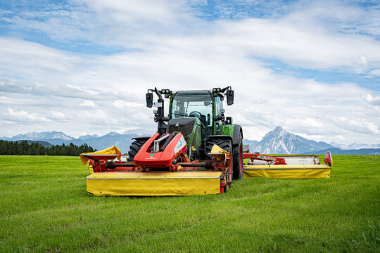 Einsatzbereiter Fendt Schlepper mit drei angebauten Kreiselm&auml;hern von P&ouml;ttinger vor Alpenpanorama.