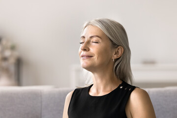 Close up mature woman closing her eyes resting seated on sofa at home, taking break from daily...