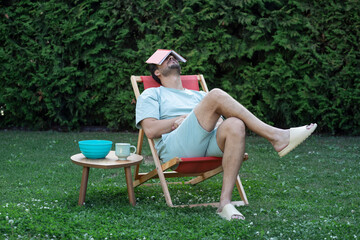 Engaged man sitting on a sun lounger on the lawn and reading a book	
