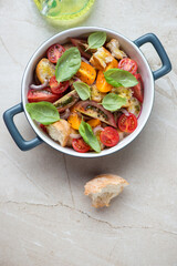 Serving pan with italian panzanella salad on a beige stone background, vertical shot with space, top view