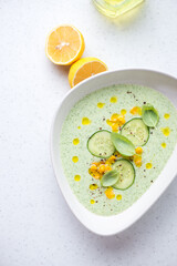 Bowl with chilled cucumber and sweet corn soup, top view on a white stone background, vertical shot