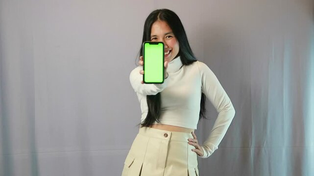 Chic woman in white top and beige skirt shows smartphone with green screen, ready for customization.