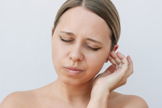 Young caucasian woman pressing on the ear trying to get rid of congestion on a light background. The problem of sulfur plugs. The girl suffering from ear pain