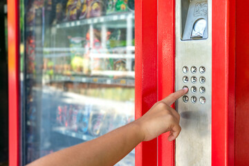 Close up of a girl's hand selecting a snack or a refreshment to buy on an automated vending machine.
