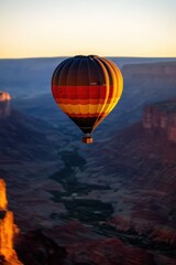 Obraz premium A vibrant hot air balloon floats above a majestic canyon at sunrise, creating a stunning landscape view filled with rich colors.