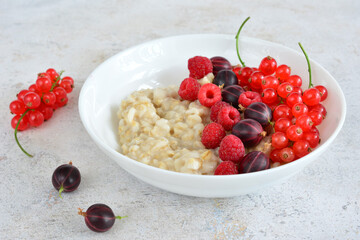 a bowl of oatmeal with raspberries, currant and purple gooseberries
