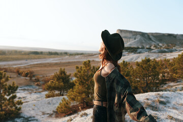 Woman in hat and plaid shirt standing on hill gazing at horizon on sunny day