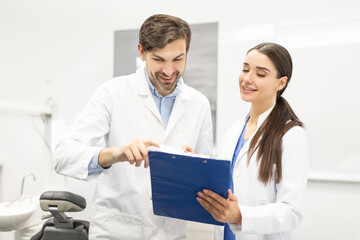 Obraz premium Male dentist doctor and his female assistant looking and discussing medical results on clipboard in modern dental clinic interior