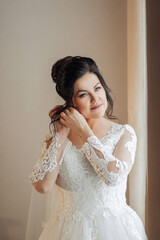 A woman is getting ready for a wedding and is putting on her wedding dress. She is looking at herself in the mirror and she is in a good mood