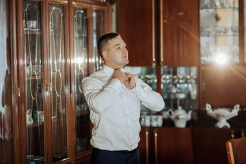 A man in a white shirt is getting dressed in front of a cabinet. Concept of formality and preparation for a special occasion
