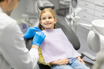 Dentist preparing to conduct teeth-polishing procedure or checkup to little female patient, girl...