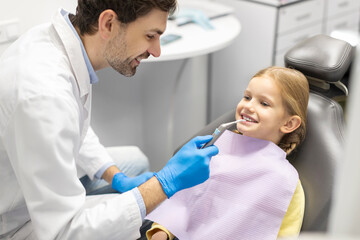 Obraz premium Professional hygiene for child teeth. Male dentist examining and consulting kid girl patient in dentistry clinic office