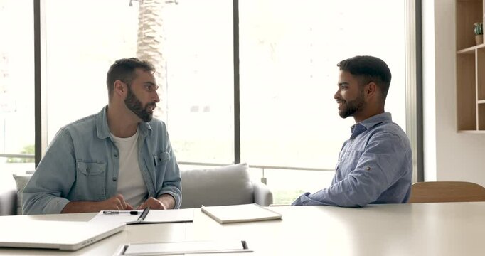 Two happy multiethnic male business partners making fist bumps gesture at office table, discussing teamwork success, successful cooperation, enjoying office friendship, effective partnership