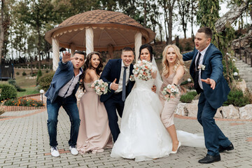 A group of people posing for a picture, including a bride and groom. The bride is holding flowers and the groom is holding a camera. Scene is happy and celebratory