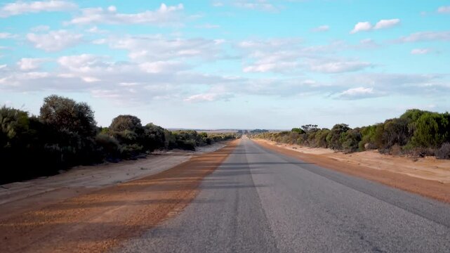 campervan driving a long road in the Australian Outback in Western Australia. You can see the vast landscape and just how remote the road is.