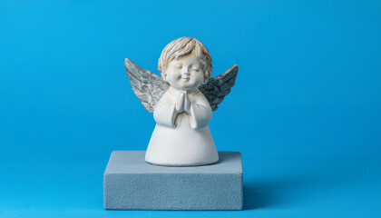 Obraz premium Ceramic figurine of cute sleeping angel on gray podium on blue background.
