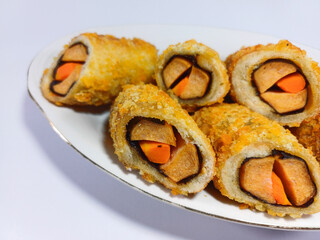 Deep-Fried Sausage Rolls Made of Chicken Sausage, Nori, and Carrots Wrapped in Bread Coated in Breadcrumbs, Placed on a White Dish Against a White Background: A Crispy and Flavorful Snack Displayed