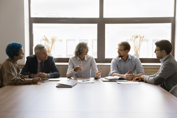 Five young and mature multiethnic staff engaged in briefing at conference table. Shareholders...