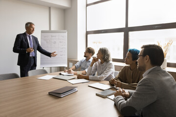 Mature business trainer interacts with participants during educational training in conference room,...
