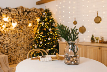 Christmas tree is lit up with lights in front of wall of wood. Vase with green plant on a table