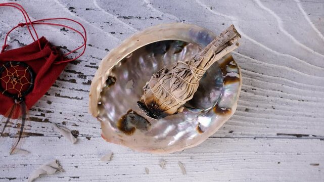 Burning a white sage smudge stick using a smudging feather to waft the cleansing smoke