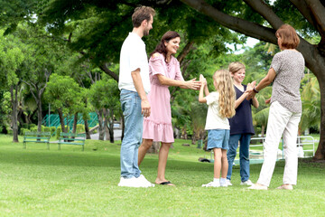 Happy cheerful family spend time together outside at public green park, playing patty cake. Father, mother, daughter girl, son boy and elderly grandma in summer garden. Joyful kid, parents and senior