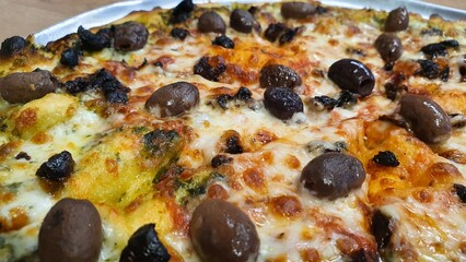 Whole Pizza with Cheese, Whole Black and Brown Olives, and Tomato Sauce on Round Tray on Wooden Table