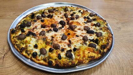 Whole Pizza with Cheese, Whole Black and Brown Olives, and Tomato Sauce on Round Tray on Wooden Table