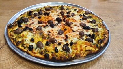 Whole Pizza with Cheese, Whole Black and Brown Olives, and Tomato Sauce on Round Tray on Wooden Table