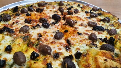 Whole Pizza with Cheese, Whole Black and Brown Olives, and Tomato Sauce on Round Tray on Wooden Table