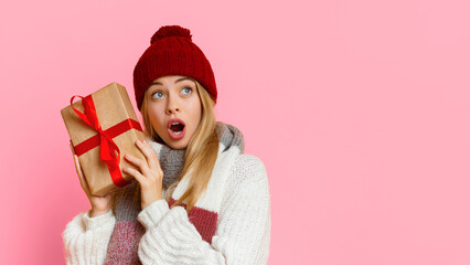 New Year, Christmas gifts, presents concept. Surprised young winter girl with new year gift looking at free space over yellow background