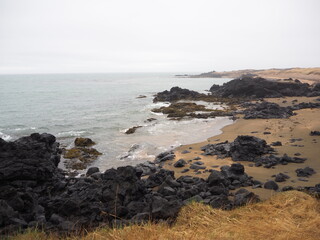 Waves roll over black volcanic rocks scattered along this sandy beach, creating a sense of serene...