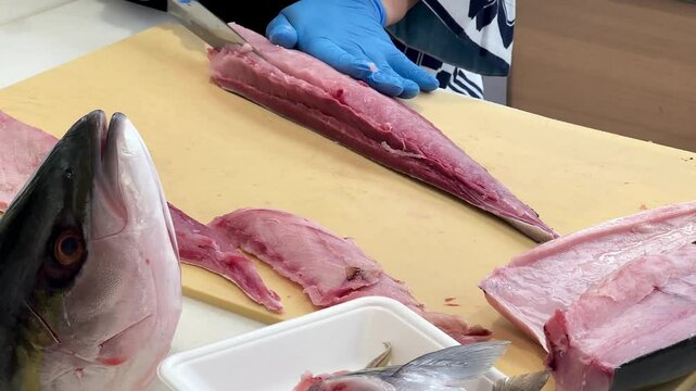 4K Chef skillfully fillets Hamachi fish, with the fish head visible in front of him as he fillets the fish on a cutting board to serve to customers.