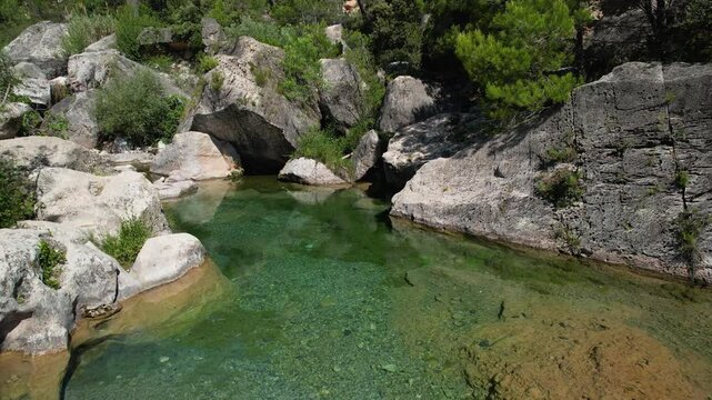 Forward reveal aerial shot of small pool on the Brugent river on sunny summer day. La Riba, Tarragona, Spain.