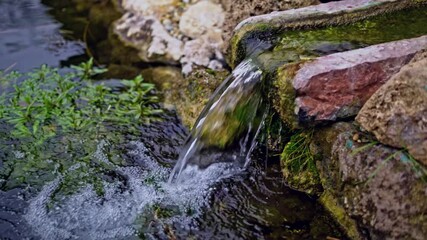 Peaceful tranquil meditation garden with fountain and pool of water. Old mossy rustic stone wall. Idyllic tranquil outdoor setting with splashing waterfall. Slow motion video.