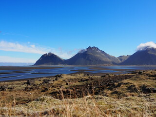 Spectacular snow-capped mountains rise against a clear blue sky, overlooking expansive wetlands, creating a stunning natural panorama that evokes a sense of adventure and peace.