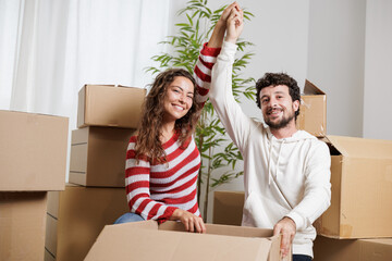 Happy and smiling young couple in their new house. They are opening the caryon boxes with their belongings to start their new life together after their honeymoon. Real estate, home sales.