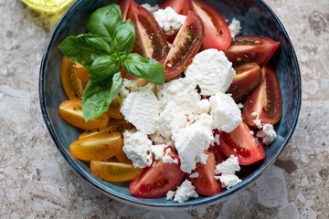 Salad with heirloom tomatoes, ricotta cheese and green basil served in a blue bowl, horizontal shot, middle closeup