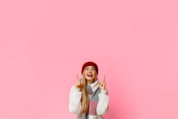 Amazed girl in red winter hat pointing up at copy space over yellow background