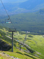 A scenic chairlift spanning over a vast, green valley with distant mountains in the background,...