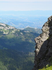 An expansive view over a lush green valley towards distant mountain ranges and a far-off city,...