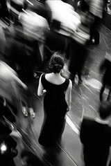 Blurred image of a woman in black dress in a crowd of moving people. Black and white image of a woman in a crowd with motion blur and high grain.